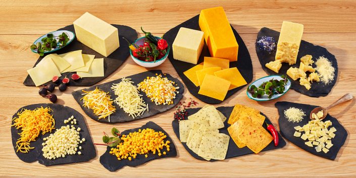 Produktfoto von verschiedenen Käsesorten der Firma Dairygold. angerichte auf Schieferplatten auf heller Holz-Küchenplatte.